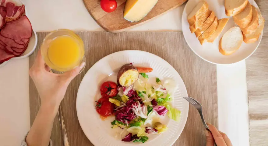 Persona disfrutando una ensalada, tomates, patata asada y un vaso de zumo, parte de su dieta intermitente 16/8.