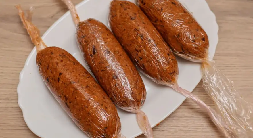 Cuatro chorizos veganos envueltos en plástico transparente, listos para cocinar.