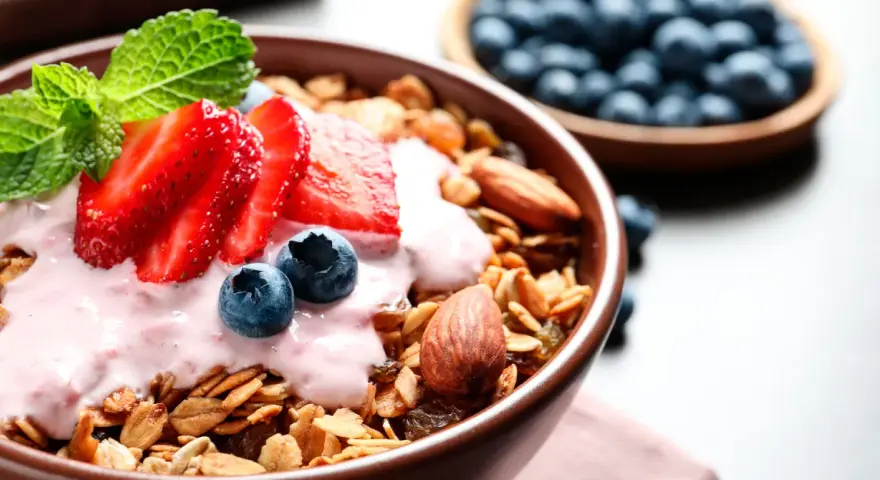 Un tazón de qué es la granola, cubierto con yogur de fresa, fresas, arándanos y almendras.
