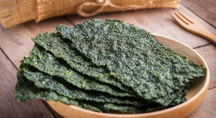 Plato de madera con finas láminas de varios tipos de algas comestibles, listas para disfrutar.