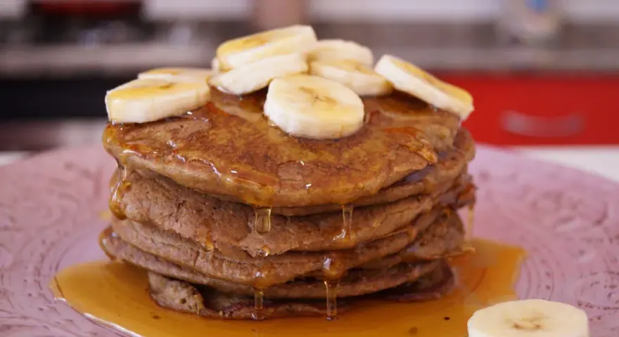 Pila de tortitas de avena y plátano, cubiertas con rodajas de plátano y sirope dorado. ¡Un desayuno delicioso!