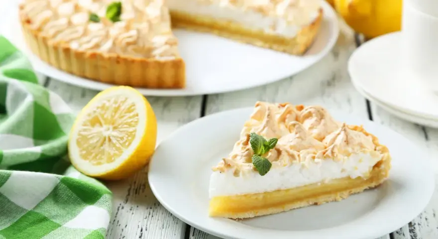 Un delicioso pastel de limón con merengue dorado, acompañado de limones frescos y una servilleta a cuadros verdes. Los ingredientes del lemon pie lucen perfectos.