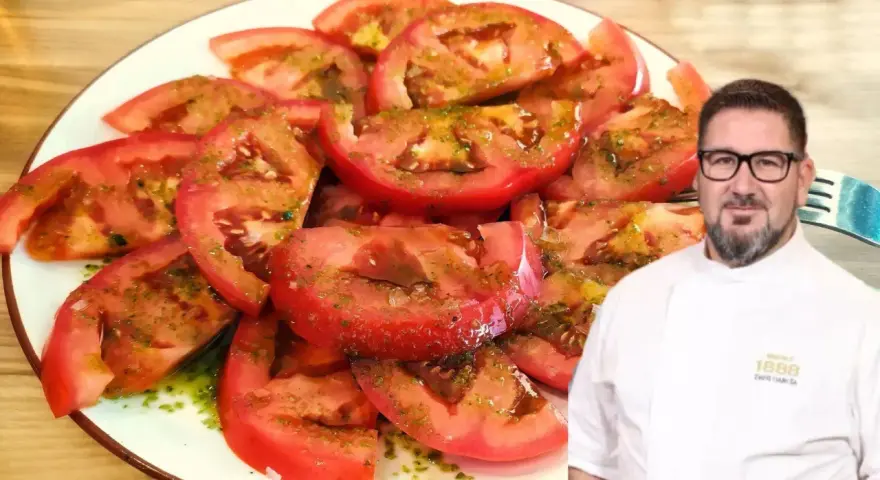 Un chef sonriente presenta un plato de tomate aliñado, fresco y jugoso, con un aderezo verde y aceite.