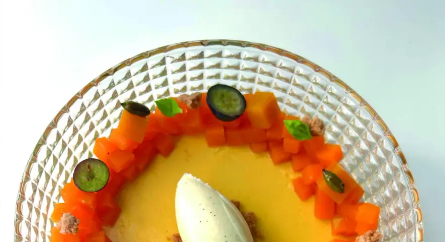 Delicioso flan de mango con helado de vainilla, trozos de mango fresco, arándanos y hojas de menta en un plato de cristal.