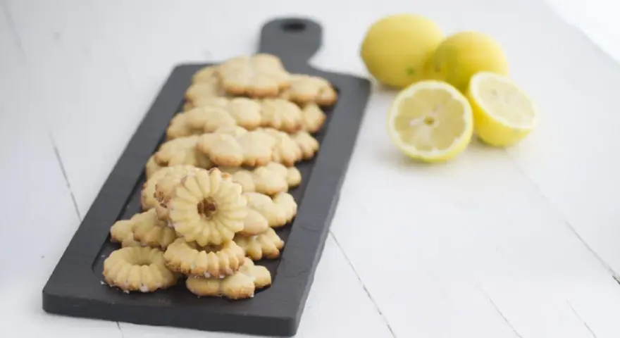 Deliciosas galletas de limón dispuestas en una tabla negra, con limones frescos al lado.