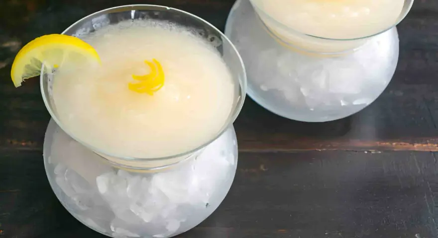 Dos copas de sorbete de limón, una con rodaja de limón y rizo de piel, servidas sobre hielo picado.