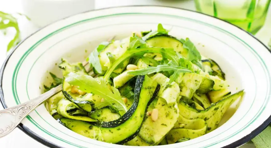 Deliciosa ensalada de calabacín en espiral con pesto y rúcula, adornada con piñones. Un plato fresco y vibrante.