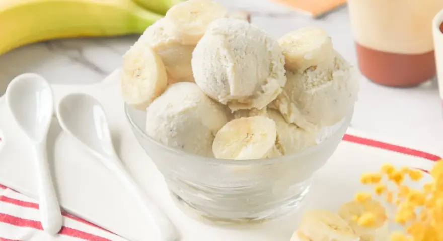 Delicioso helado de platano casero, cremoso y refrescante, servido en un cuenco de cristal con rodajas de plátano fresco.