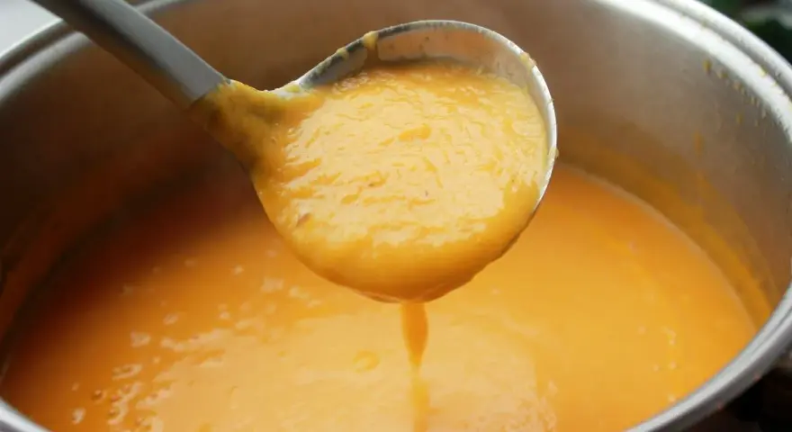 Cucharón sirviendo una deliciosa crema de zanahoria y puerro recién hecha de una olla.