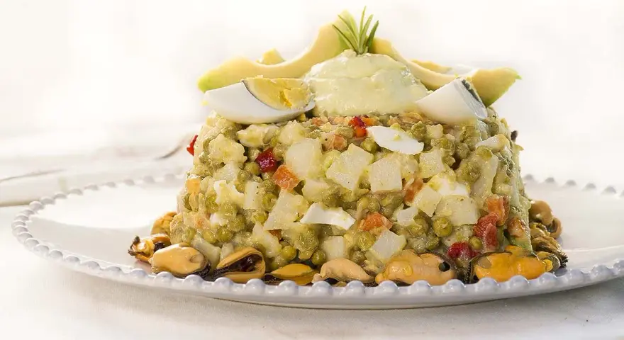Deliciosa ensaladilla de aguacate con huevo duro, guisantes y mejillones, coronada con una crema suave y rodajas de aguacate fresco.