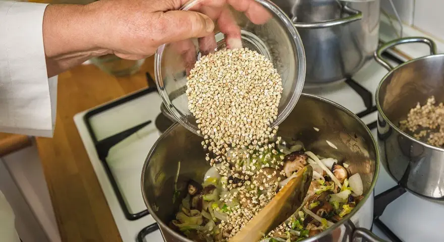 Mano añade trigo sarraceno a una olla con verduras y champiñones.