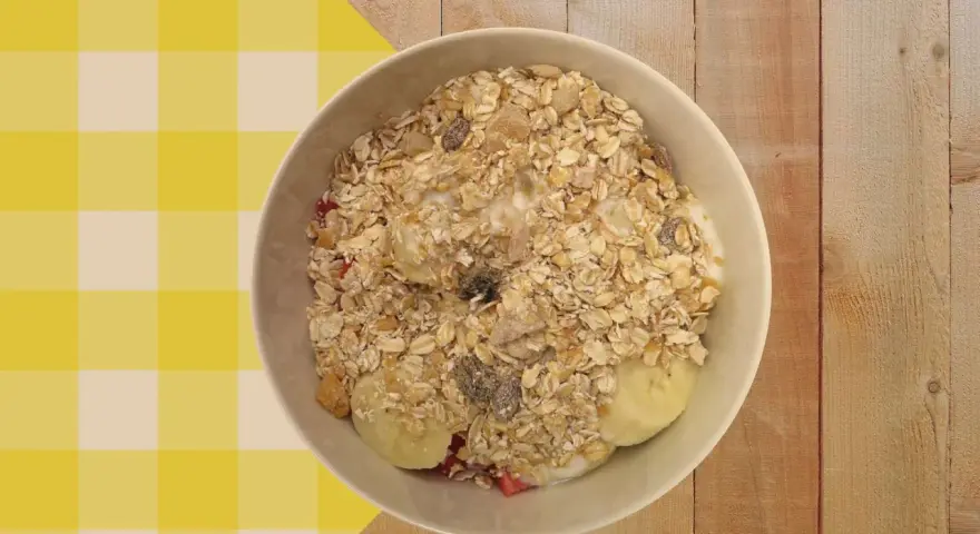 Un tazón de porridge de avena con plátano, fresas y pasas, servido sobre un mantel a cuadros amarillos y blancos.