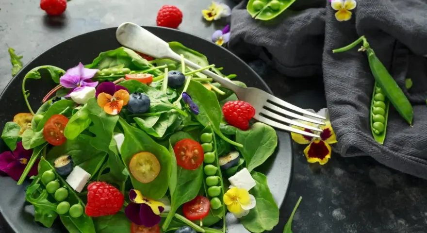 Ensalada vibrante con frambuesas, arándanos, guisantes y flores comestibles, celebrando las frutas de primavera.