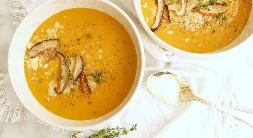 Dos tazones de cremosa sopa de calabaza, adornados con champiñones y queso rallado, listos para ser disfrutados.