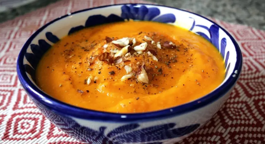 Crema de zanahoria y jengibre, servida en un cuenco azul y blanco, adornada con nueces y pimienta.