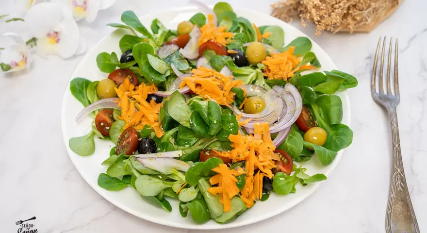 Deliciosa ensalada mediterránea con lechuga, tomate, aceitunas, cebolla morada y zanahoria rallada.