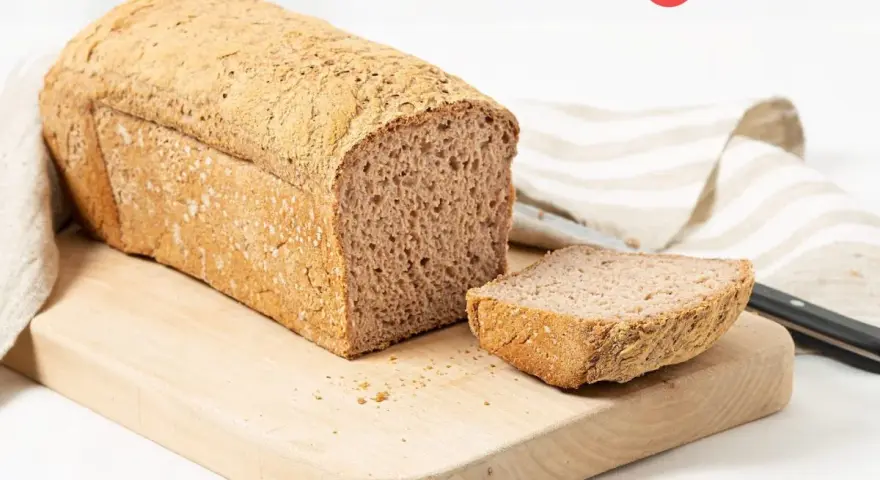 Pan sin gluten recién horneado, con una rebanada lista para disfrutar. Su textura porosa y corteza dorada invitan a probarlo.