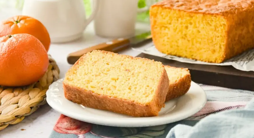Un delicioso bizcocho de mandarina, recién horneado, con dos rebanadas servidas en un plato blanco.