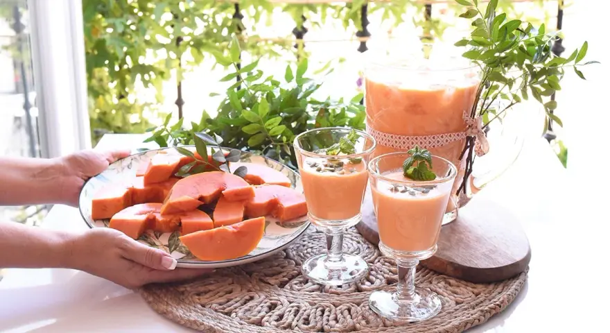 Delicioso zumo de papaya servido en copas y jarra, acompañado de papaya fresca en rodajas.