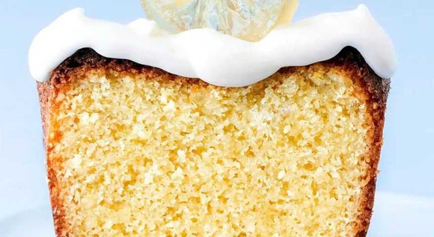 Rebanada de bizcocho esponjoso con un delicioso frosting de limón y una rodaja de limón cristalizado encima.