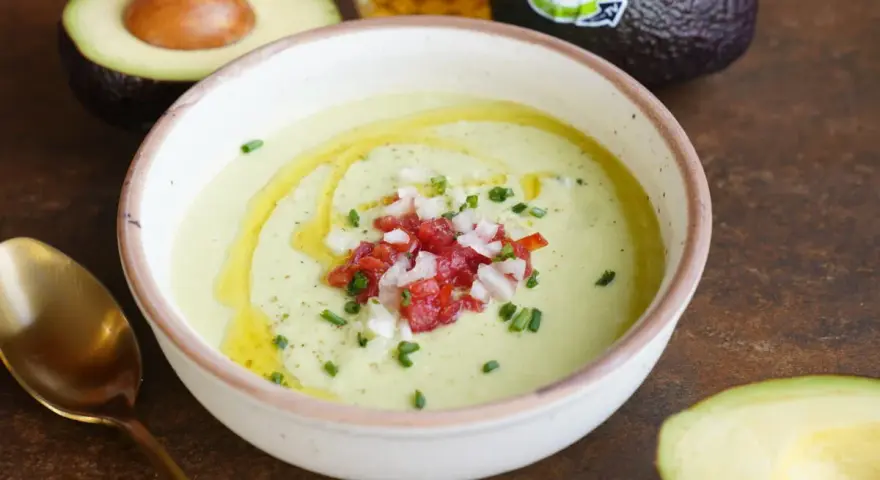 Un cremoso gazpacho de aguacate, adornado con tomate picado, cebolla y cebollino, con un chorrito de aceite de oliva.