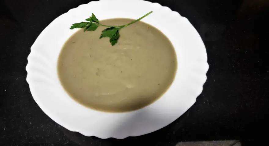 Crema de berenjena suave y sedosa, decorada con una ramita de perejil fresco, lista para disfrutar.