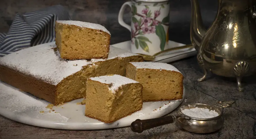 Un delicioso bizcocho de mango, espolvoreado con azúcar glas, listo para disfrutar con una taza de té.