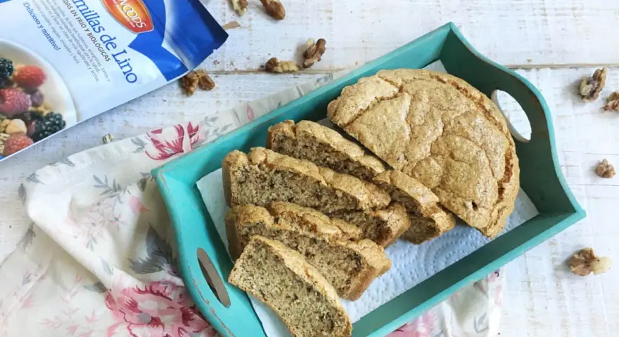 Rebanadas de pan de lino en una bandeja turquesa, junto a un paquete de semillas de lino y nueces.