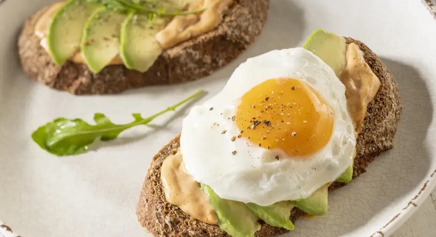Tostas de aguacate para cenar, una con huevo frito y la otra con rúcula. Delicioso y saludable.
