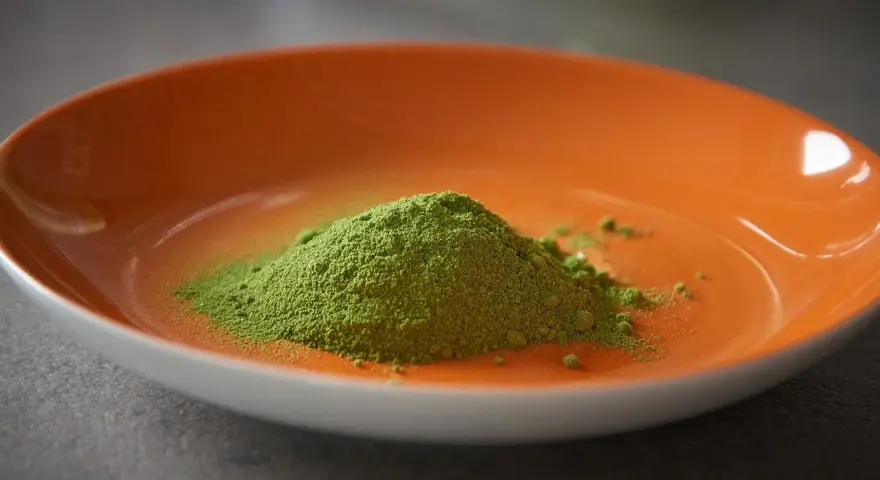 Montículo de polvo verde vibrante, polvo de moringa, en un plato naranja brillante.