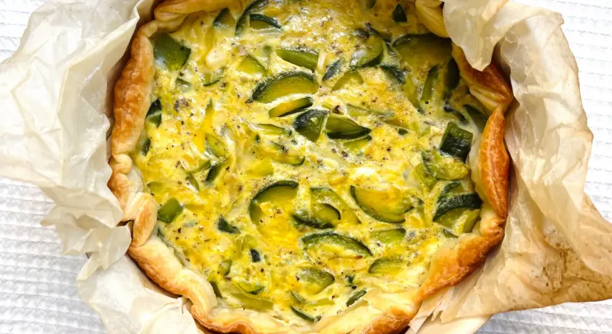 Quiche de calabacín recién horneada, con masa dorada y relleno cremoso salpicado de trozos verdes.