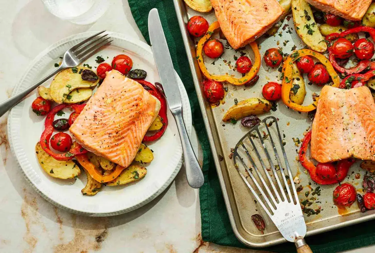 Salmón al horno con verduras: patatas, pimientos y tomates cherry asados, servidos en un plato y en una bandeja.