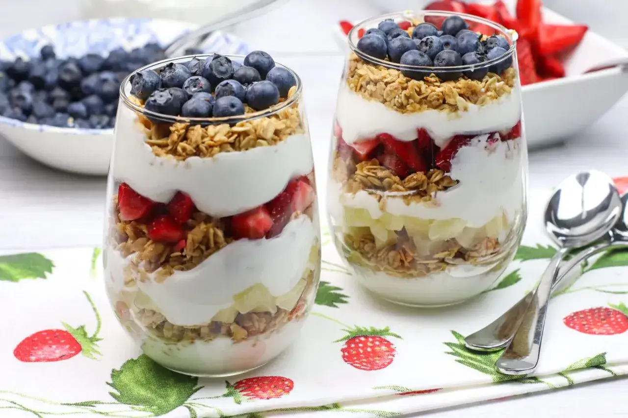 Dos vasos con capas de yogur, fresas, arándanos y qué es la granola, un desayuno saludable y delicioso.