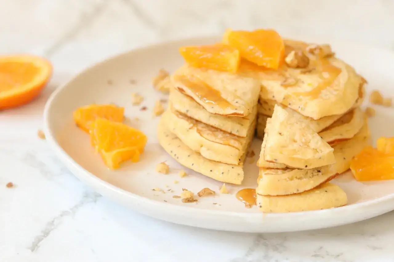 Deliciosos pancakes sin gluten con trozos de naranja y sirope dorado.