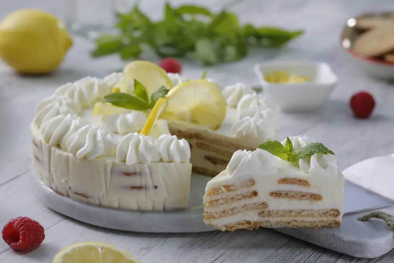 Delicioso pastel de dulce de limón, cubierto de crema batida y decorado con rodajas de limón y menta.