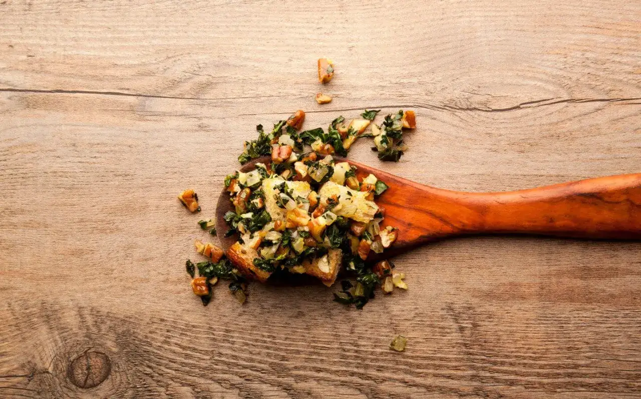 Cuchara de madera con ensalada de col kale, pan tostado y nueces sobre una mesa de madera.