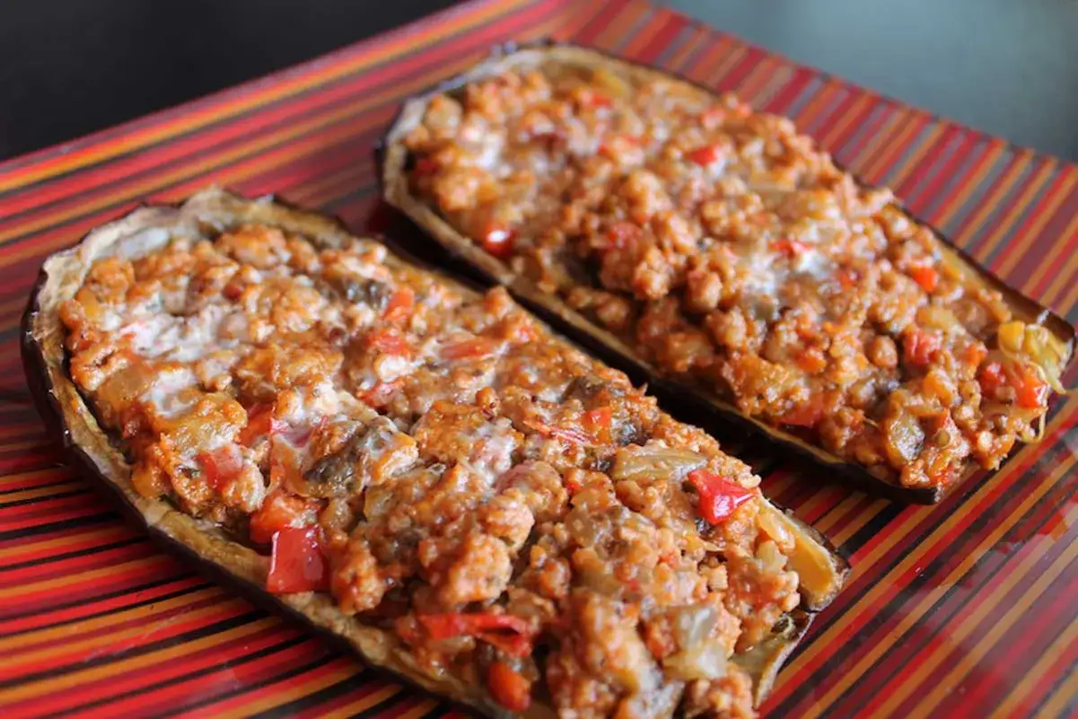 Dos mitades de berenjena rellena, doradas y jugosas, reposan sobre un plato de rayas vibrantes.
