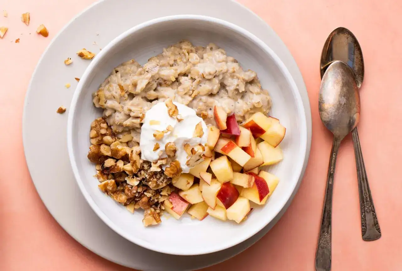 Un taz&oacute;n de porridge cremoso con nueces picadas, trozos de manzana y una cucharada de yogur. Un desayuno saludable y delicioso.