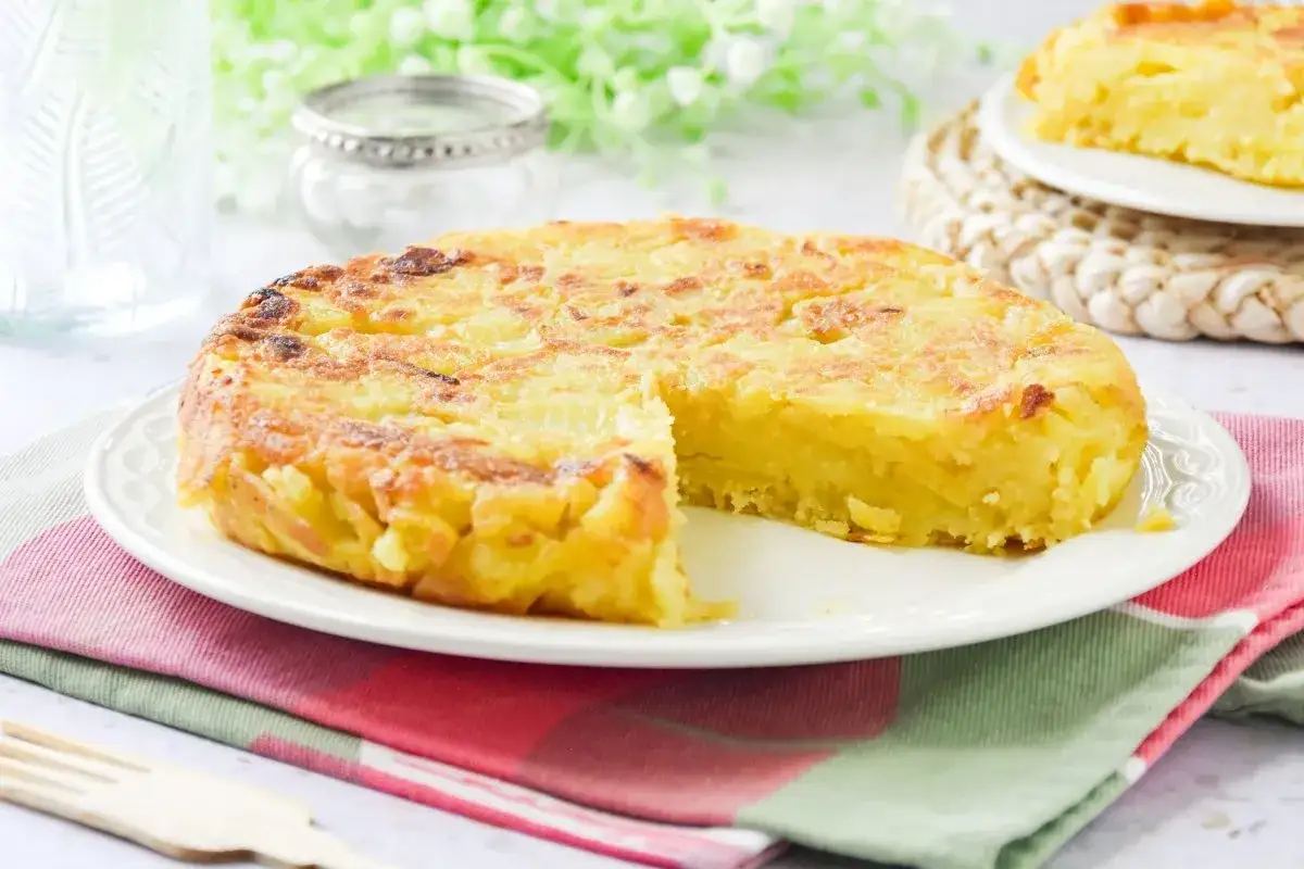 Deliciosa tortilla vegana de patatas, dorada y jugosa, servida en plato blanco.