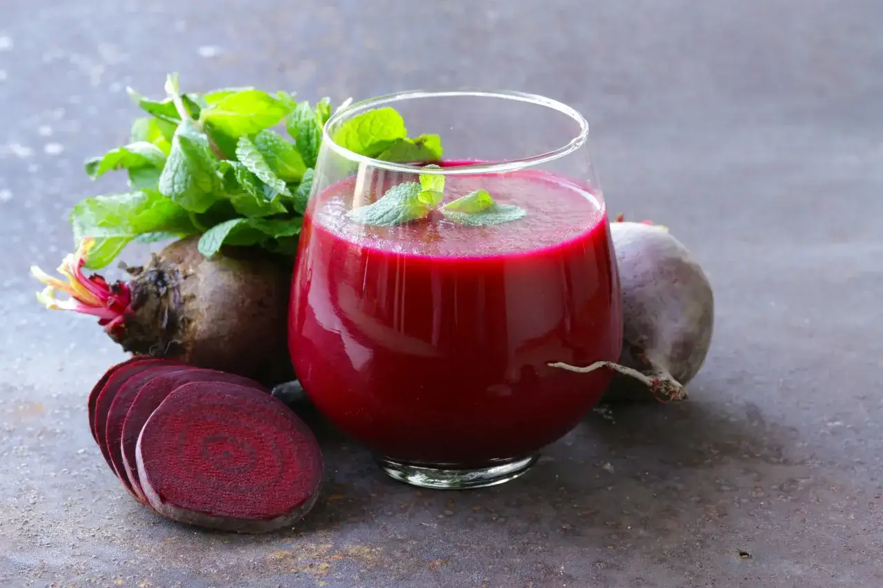 Vaso de zumo de remolacha con menta, acompa&ntilde;ado de remolachas enteras y cortadas. Ideal como zumos para la anemia.