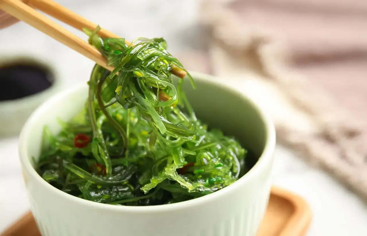 Palillos recogen ensalada de algas, un ejemplo de tipos de algas comestibles, de un cuenco verde.
