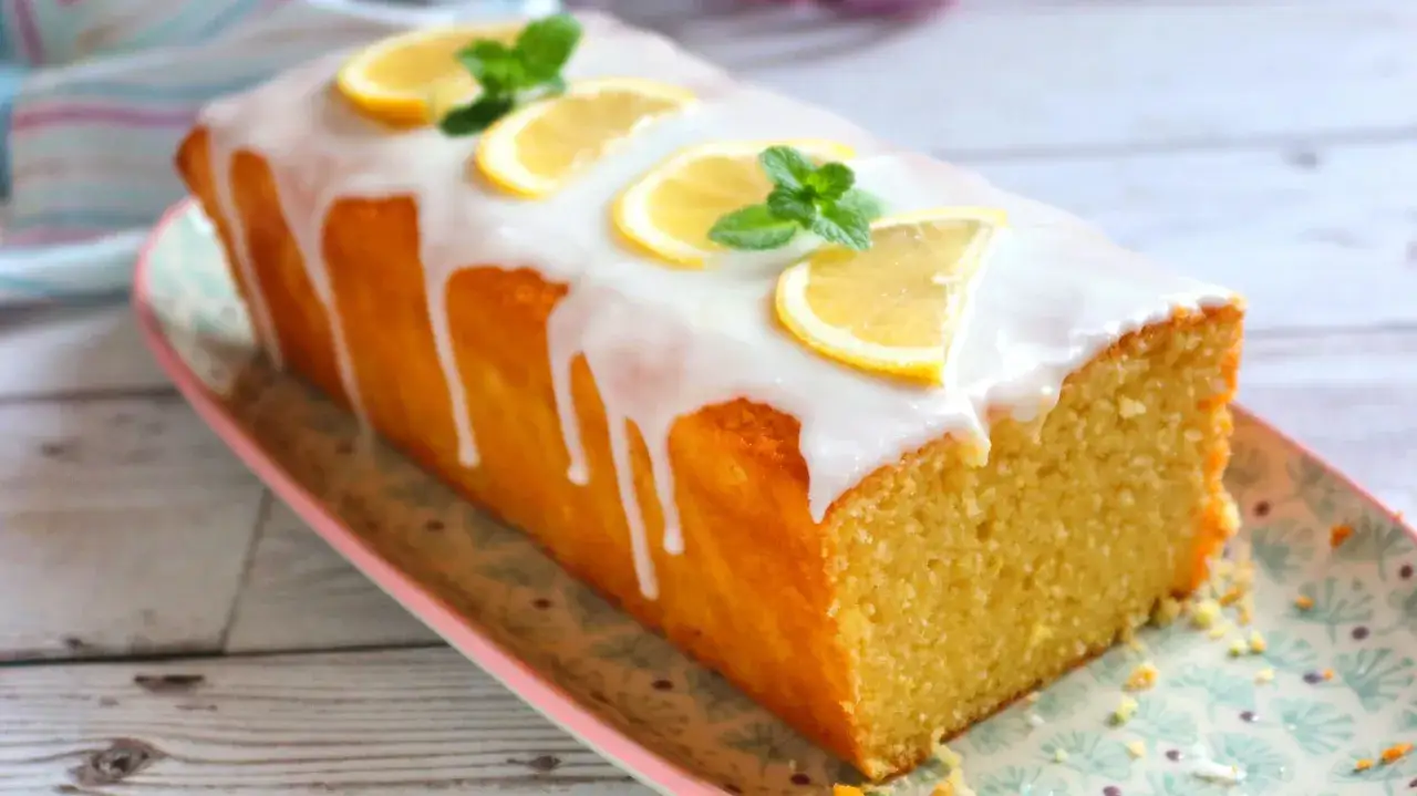 Bizcocho esponjoso con glaseado de limón, decorado con rodajas de limón y hojas de menta.