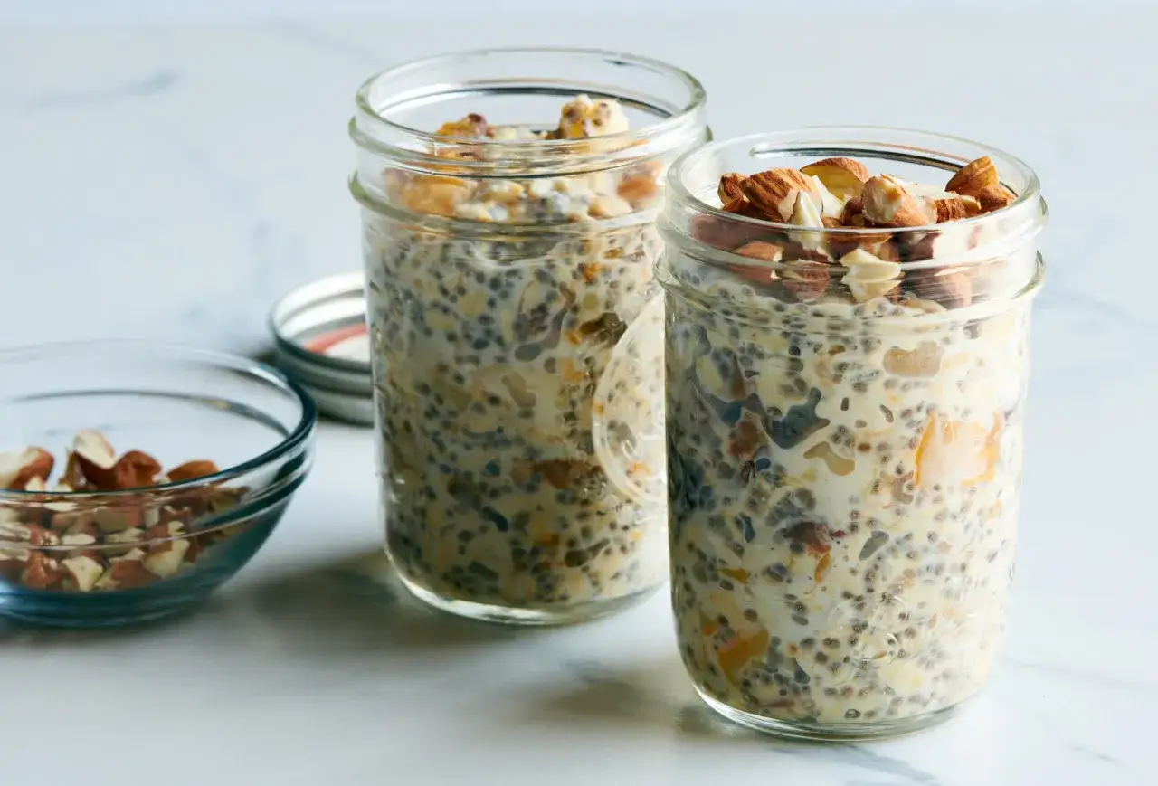 Dos frascos de avena nocturna con almendras picadas y un tazón pequeño con más almendras.