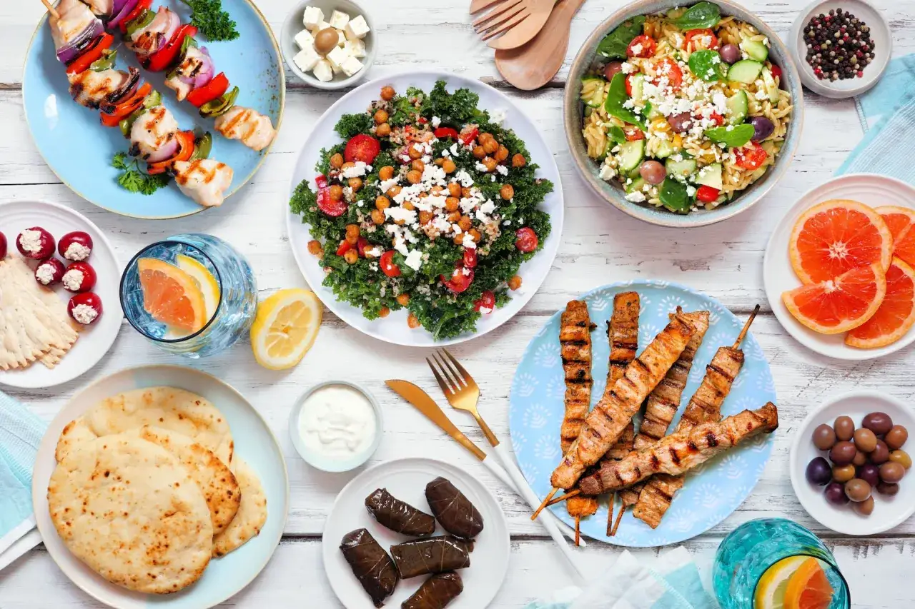 Mesa con brochetas de pollo, ensalada de kale con garbanzos y queso feta, y pinchos de carne. Una comida rica en prote&iacute;nas vegetales y otros ingredientes frescos.