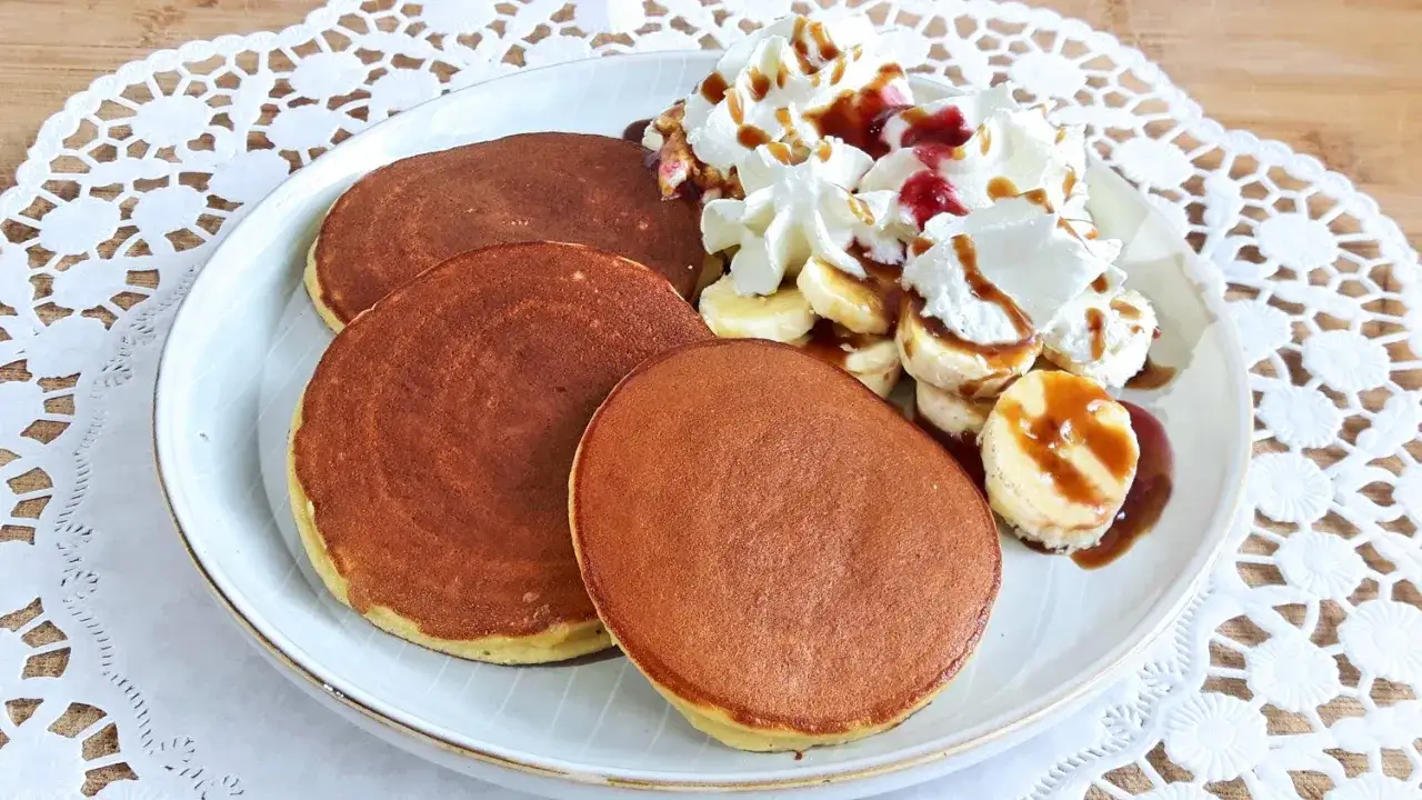 Panqueques dorados con plátano, crema batida y sirope. ¡Un delicioso desayuno que demuestra que pan no tiene gluten puede ser increíble!