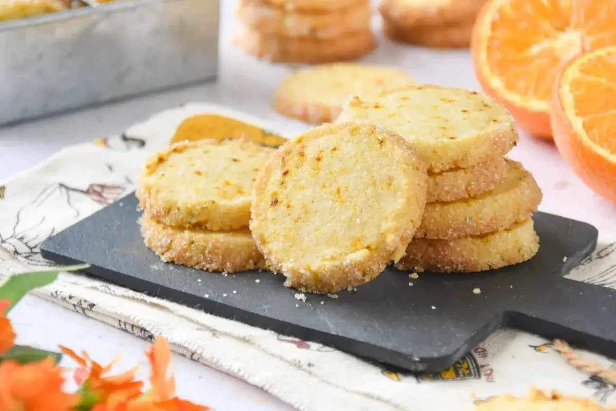Deliciosas galletas de naranja, crujientes y con un toque c&iacute;trico, apiladas sobre una tabla negra.