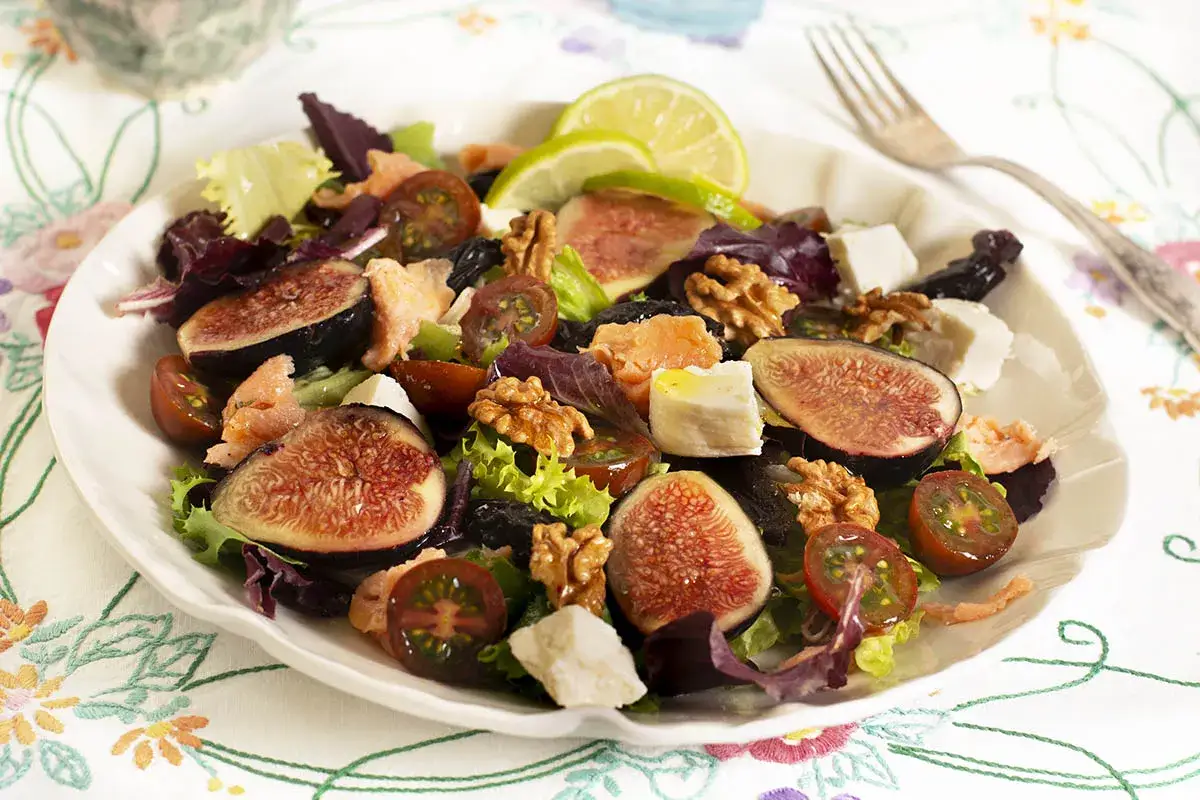 Ensalada con higos cortados, queso feta, nueces, tomates cherry y salmón. Una delicia que muestra como se hacen los higos en una ensalada.