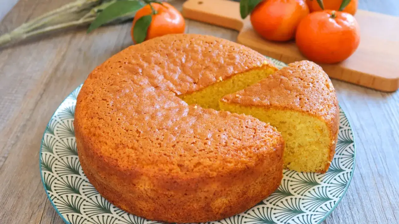 Bizcocho de mandarina esponjoso y dorado, con una porci&oacute;n cortada, listo para disfrutar.