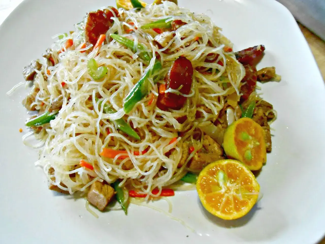 Deliciosa receta con noodles de arroz, salteados con verduras, carne y salchicha, adornado con gajos de mandarina.