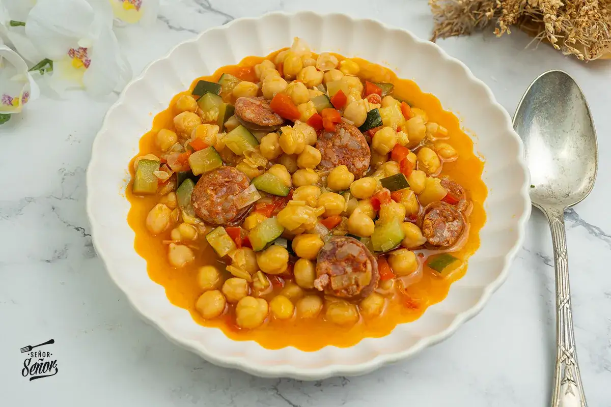 Plato de garbanzos con chorizo, calabacín y pimiento rojo. Una deliciosa receta de garbanzos tradicional, servida en un cuenco blanco.